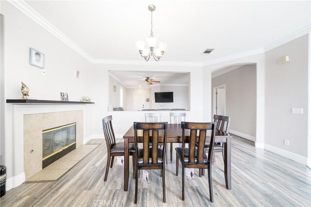 dining room featuring ceiling fan with notable chandelier, a fireplace, ornamental molding, and light hardwood / wood-style flooring