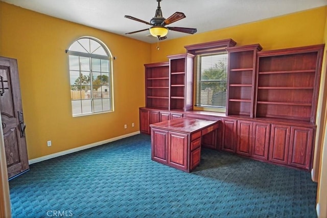 unfurnished office featuring a wealth of natural light, ceiling fan, and dark colored carpet