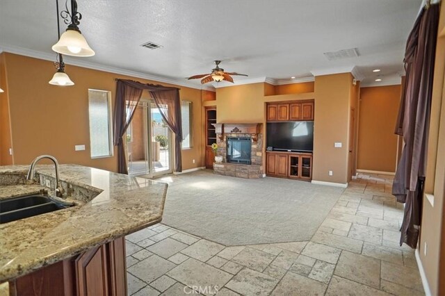 carpeted living room featuring ceiling fan, sink, a stone fireplace, crown molding, and a textured ceiling