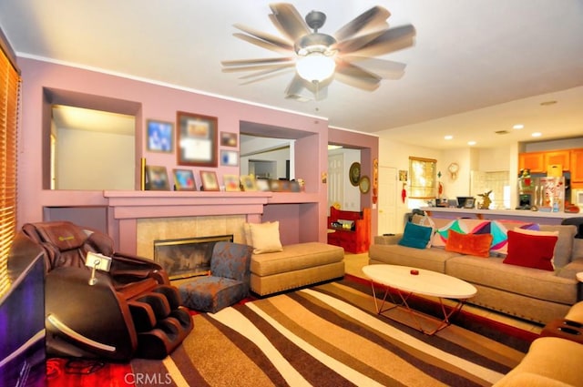 living room featuring ceiling fan, a tiled fireplace, carpet, and crown molding