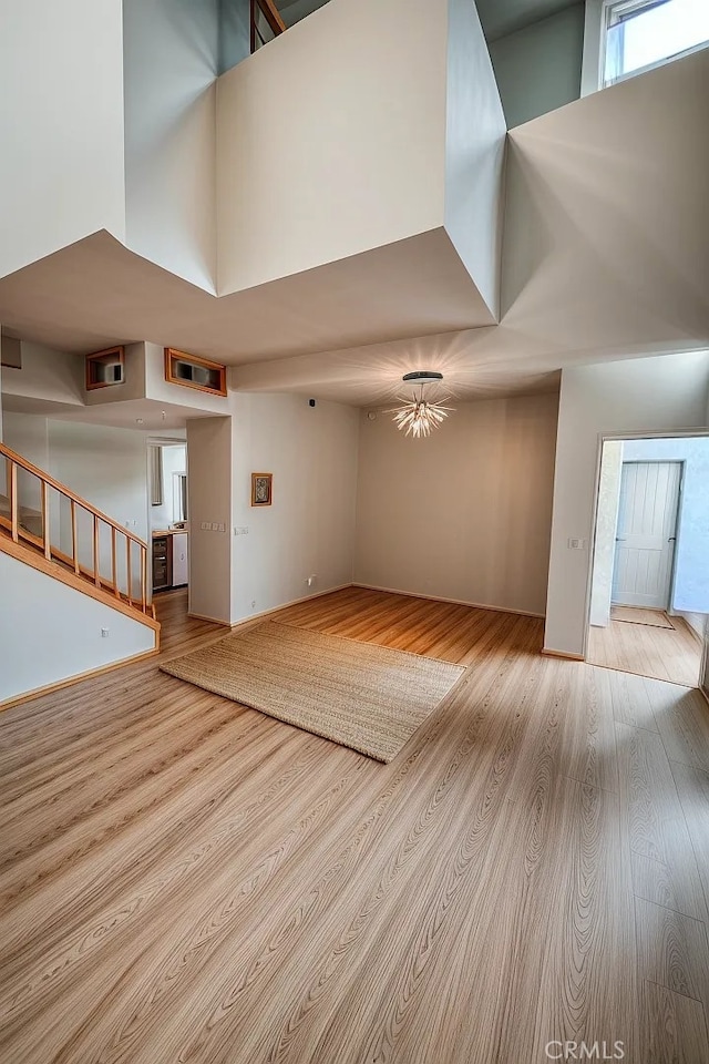 unfurnished living room featuring a notable chandelier, light wood-type flooring, and a towering ceiling