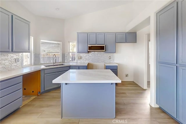 kitchen with a kitchen island, gray cabinetry, tasteful backsplash, sink, and light hardwood / wood-style flooring