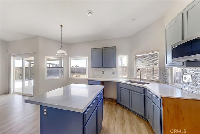 kitchen featuring decorative light fixtures, a center island, decorative backsplash, sink, and light hardwood / wood-style flooring