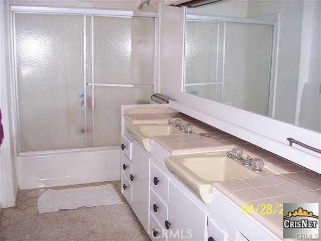 full bath featuring double vanity, shower / bath combination with glass door, and a sink