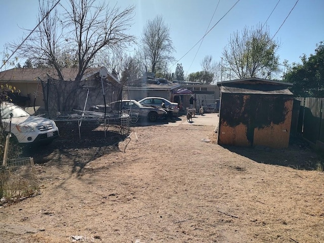 view of yard featuring a storage shed, dirt driveway, fence, and an outbuilding