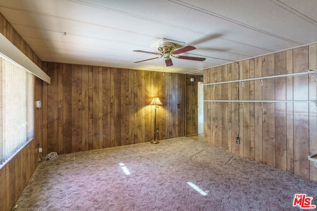 carpeted empty room with wood walls and ceiling fan