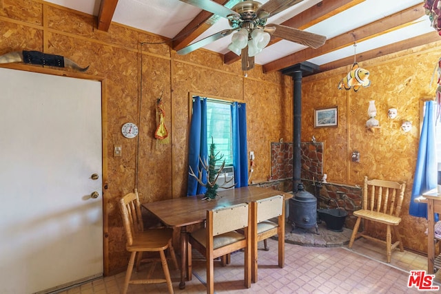 dining room with ceiling fan, beam ceiling, and a wood stove