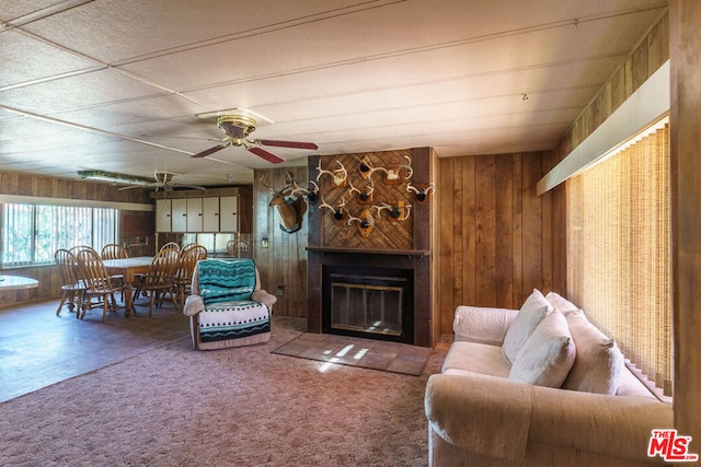 living room featuring a fireplace, carpet floors, ceiling fan, and wooden walls