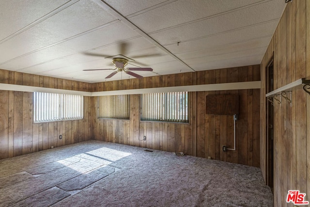 carpeted spare room featuring ceiling fan and wooden walls