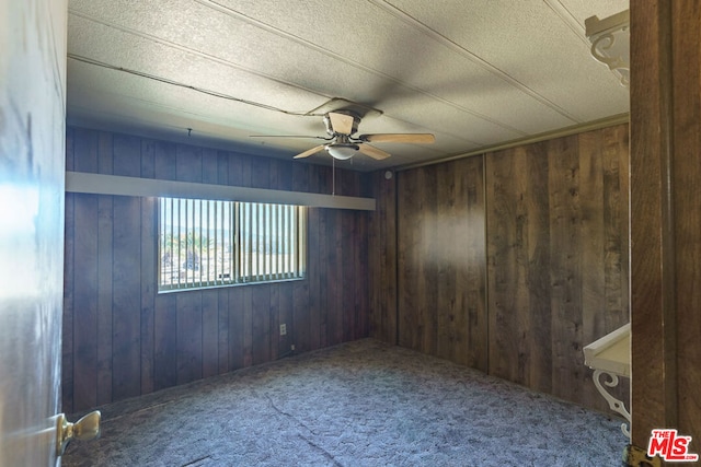 carpeted empty room featuring ceiling fan and wooden walls