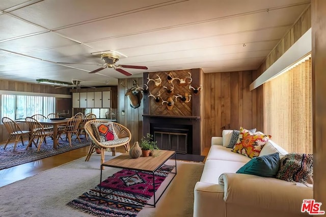 living room featuring ceiling fan, a large fireplace, and wooden walls