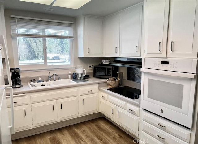 kitchen with white oven, sink, white cabinets, hardwood / wood-style floors, and black stovetop