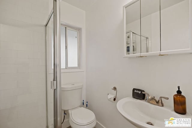 bathroom featuring toilet, a shower with shower door, and sink