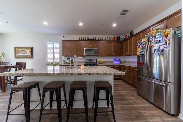 kitchen with sink, dark hardwood / wood-style floors, an island with sink, a kitchen bar, and appliances with stainless steel finishes