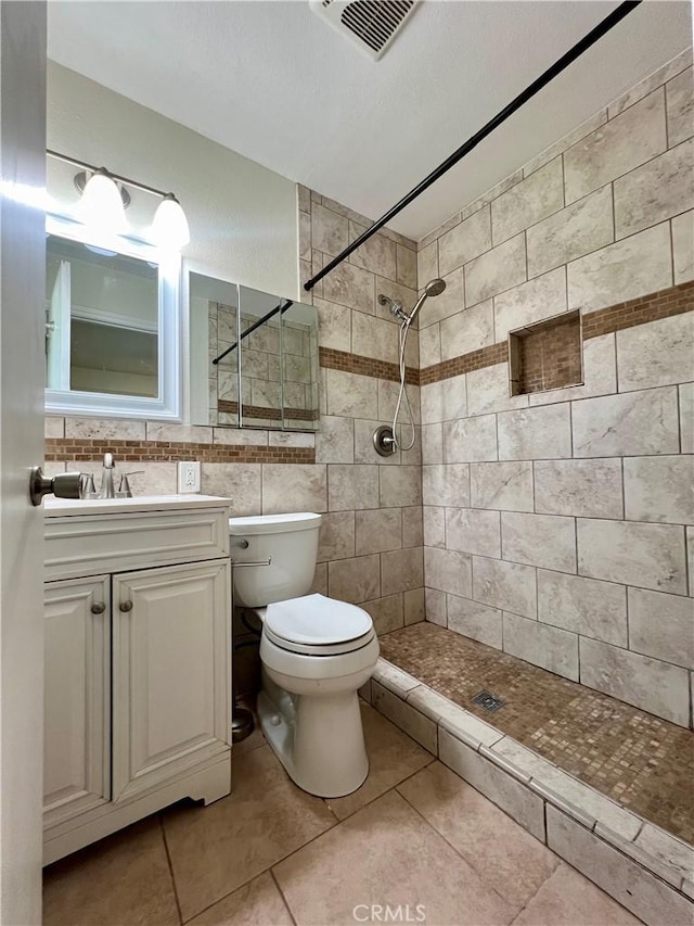 bathroom featuring tile patterned flooring, toilet, a tile shower, and vanity