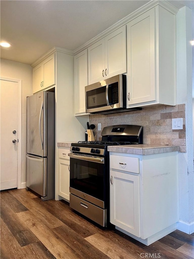 kitchen featuring white cabinets, backsplash, dark wood-type flooring, and appliances with stainless steel finishes