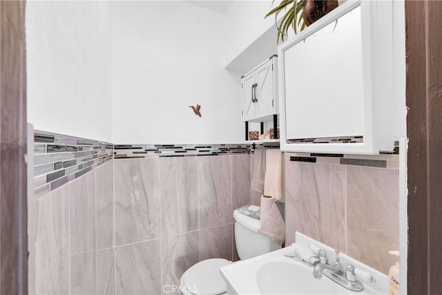 bathroom featuring toilet, tile walls, and sink