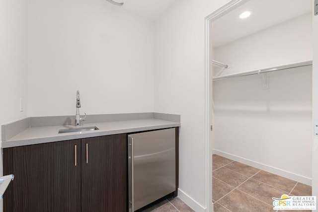 bar with stainless steel fridge, light tile patterned flooring, dark brown cabinetry, and sink