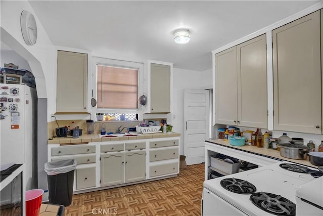 kitchen with tile counters, sink, light parquet floors, white appliances, and decorative backsplash