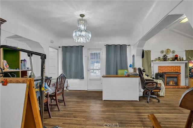 interior space featuring vaulted ceiling, dark wood-type flooring, decorative light fixtures, an inviting chandelier, and a fireplace