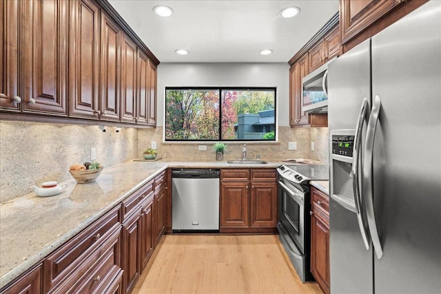 kitchen with light hardwood / wood-style floors, stainless steel appliances, decorative backsplash, light stone countertops, and sink