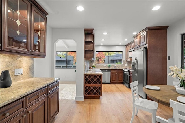 kitchen with stainless steel appliances, decorative backsplash, dark brown cabinets, light hardwood / wood-style flooring, and light stone counters