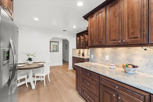 kitchen with light hardwood / wood-style floors, stainless steel fridge, decorative backsplash, light stone countertops, and dark brown cabinetry