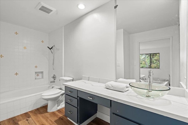 full bathroom with toilet, tiled shower / bath combo, hardwood / wood-style floors, and vanity