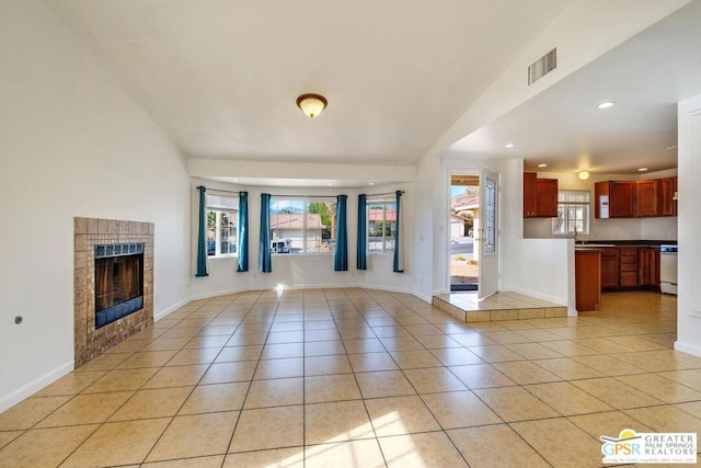 unfurnished living room with a tile fireplace, sink, light tile patterned floors, and vaulted ceiling