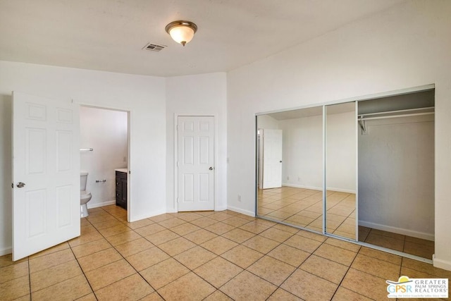 unfurnished bedroom with ensuite bath, light tile patterned floors, and a closet