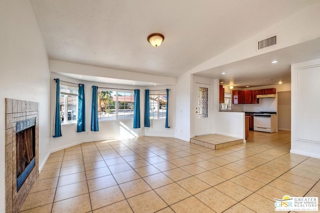 unfurnished living room with a tiled fireplace, lofted ceiling, and light tile patterned flooring