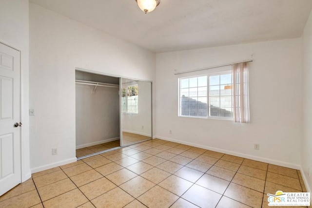 unfurnished bedroom featuring lofted ceiling, light tile patterned floors, and a closet