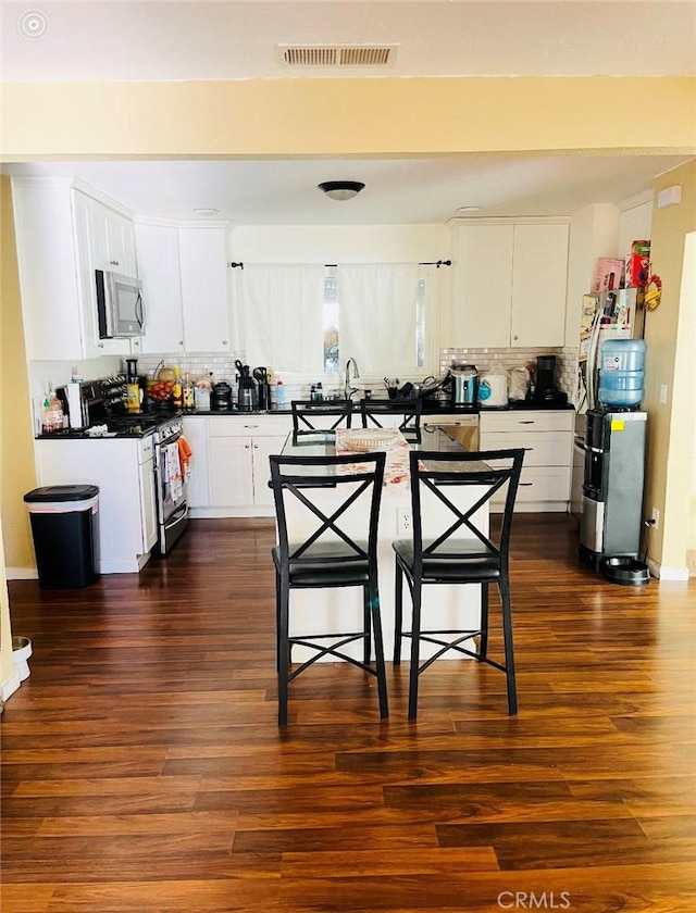 kitchen with dark hardwood / wood-style flooring, white cabinetry, a breakfast bar, and stainless steel appliances