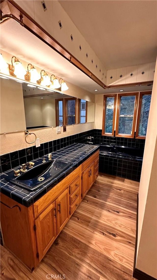 bathroom with backsplash, vanity, a bath, and hardwood / wood-style flooring