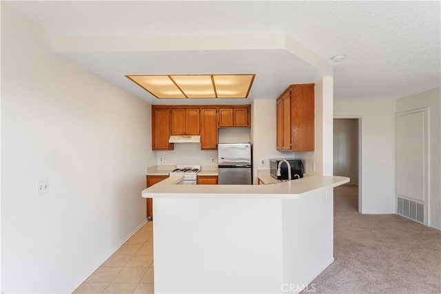 kitchen with stainless steel refrigerator, white gas range, kitchen peninsula, light colored carpet, and a textured ceiling