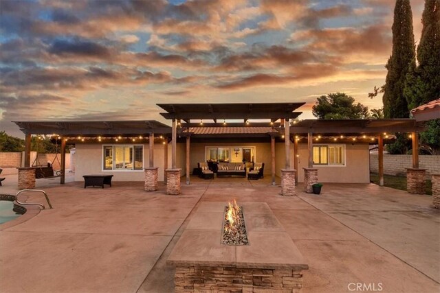 back house at dusk with a pergola, an outdoor living space with a fire pit, and a patio