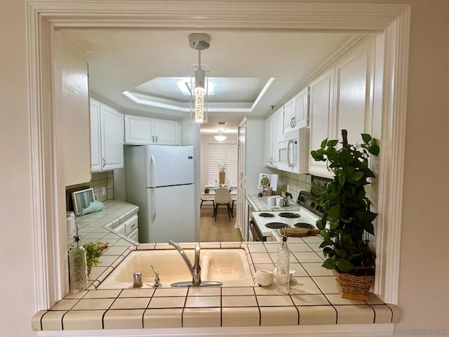 kitchen with tasteful backsplash, white appliances, a raised ceiling, white cabinets, and tile counters