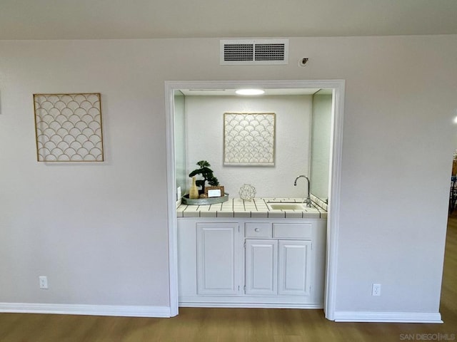 bar with white cabinets, hardwood / wood-style floors, tile countertops, and sink