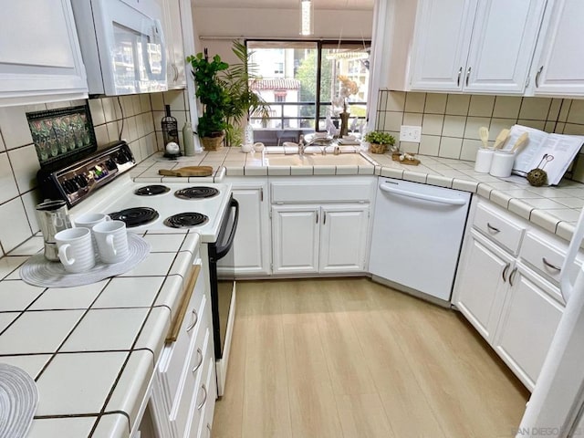 kitchen featuring backsplash, white appliances, white cabinets, light hardwood / wood-style floors, and tile counters