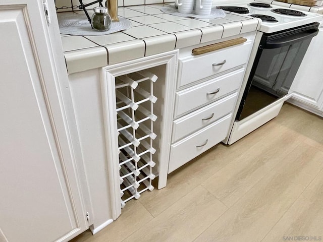 interior details featuring white cabinetry, tile counters, light hardwood / wood-style floors, and white electric range