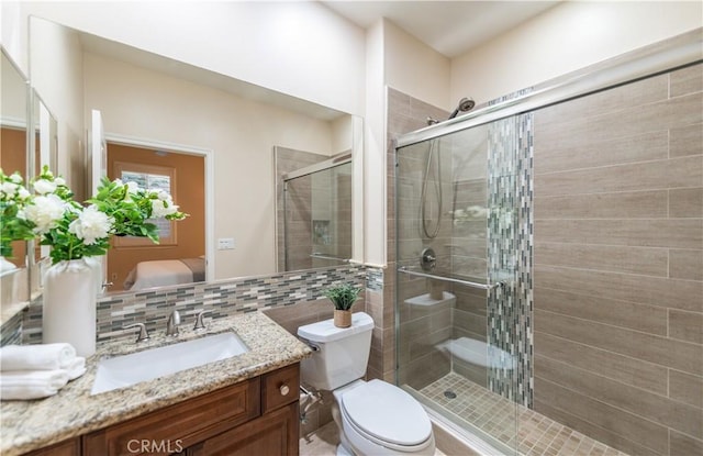 bathroom featuring vanity, toilet, a shower with door, and tasteful backsplash