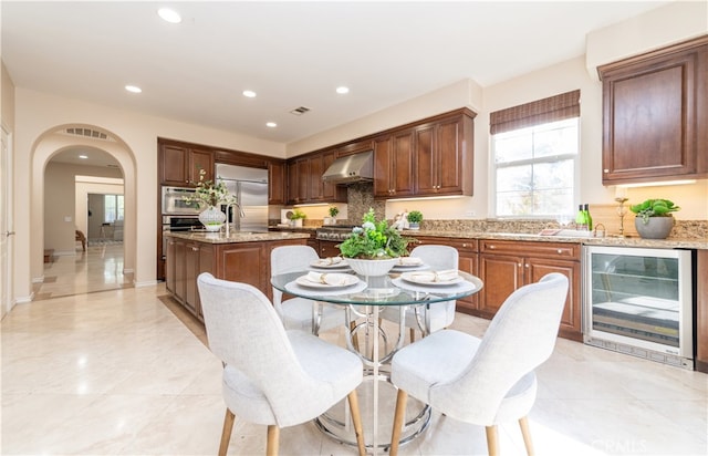 kitchen featuring a center island, beverage cooler, light stone counters, stainless steel appliances, and extractor fan