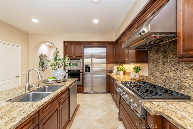 kitchen with sink, wall chimney exhaust hood, decorative backsplash, appliances with stainless steel finishes, and light stone counters