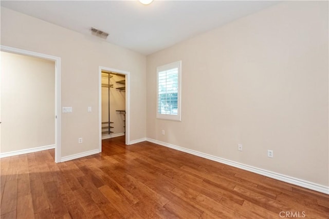 unfurnished bedroom with a spacious closet, a closet, and hardwood / wood-style flooring