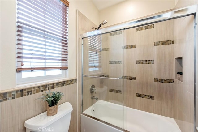 bathroom with toilet, shower / bath combination with glass door, and tile walls