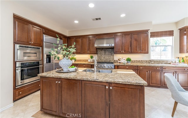 kitchen featuring sink, light stone counters, extractor fan, a center island with sink, and appliances with stainless steel finishes