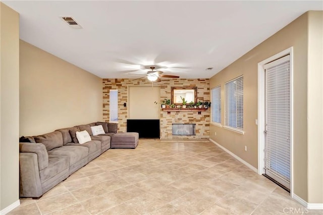 tiled living room featuring a stone fireplace and ceiling fan