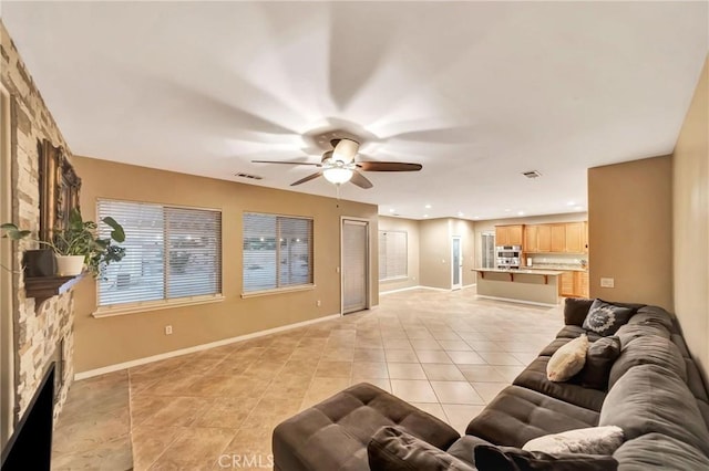 tiled living room with ceiling fan and a stone fireplace