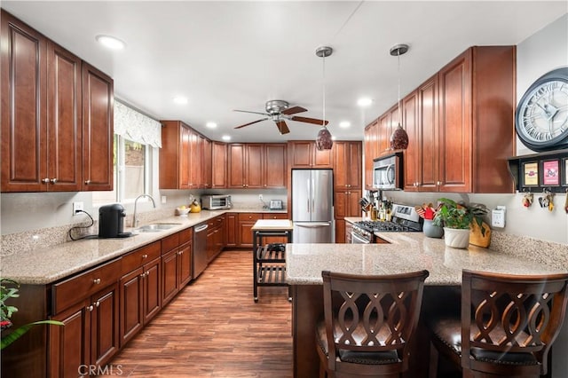 kitchen with decorative light fixtures, kitchen peninsula, sink, appliances with stainless steel finishes, and a breakfast bar area