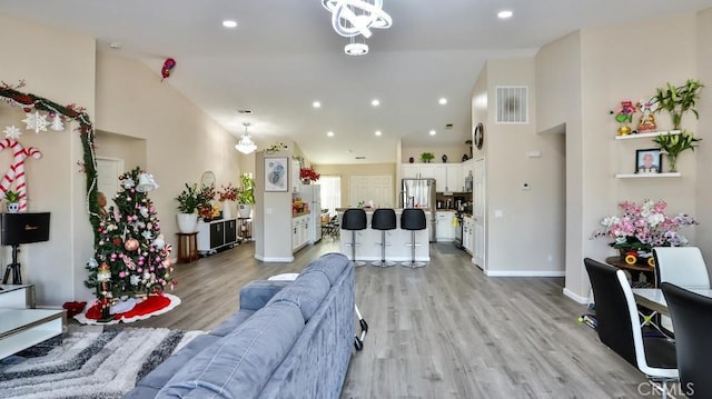 living room featuring light wood-type flooring, high vaulted ceiling, and an inviting chandelier